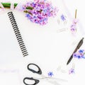 Bouquet of purple flowers, shabby tapes, clips, pen, scissors and notebook on white background. Flat lay, top view. Royalty Free Stock Photo