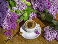 A bouquet of purple lilac flowers and a white vintage cup of coffee with a spoon on a wooden background. Royalty Free Stock Photo