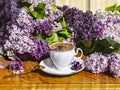 A bouquet of purple lilac flowers and a white vintage cup of coffee with a spoon on a wooden background. Royalty Free Stock Photo
