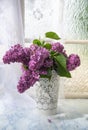 a bouquet of purple lilacs in a white openwork bucket on an old shabby window sill with a tulle curtain, romantic mood