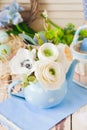 Bouquet of ranunkula in blue teapot on wooden surface