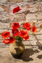 Bouquet of red poppies in clay jug on wooden table against old brick wall Royalty Free Stock Photo