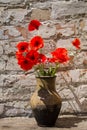 Bouquet of red poppies in clay jug on wooden table against old brick wall Royalty Free Stock Photo