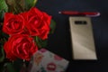 Bouquet red roses flower in glass vase on dark background and pen at the gold smartphone no focus, gift box