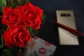 Bouquet red roses flower in glass vase on dark background and pen on the gold smartphone no focus, gift box