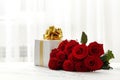 A bouquet of red roses and a gift box on the table in the interior. Love confession. Royalty Free Stock Photo