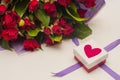 Bouquet of red roses in purple wrapping paper and gift box with red heart and purple ribbon on white background. Royalty Free Stock Photo