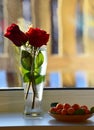A bouquet of red roses in a vase on the windowsill. Ripe tangerines with leaves in a plate.