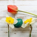 Bouquet of red spring tulip, daffodils and handmade colorful painted easter eggs against rustic wooden background