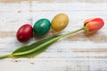 Bouquet of red spring tulip, daffodils and handmade colorful painted easter eggs against rustic wooden background