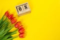 Bouquet of red tulips and cubic wooden calendar with date of 8 march and copy space on bright yellow background. Beggining of Royalty Free Stock Photo