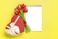 Bouquet of red tulips, gift box heart, notepad on yellow background Top view Flat lay Holiday greeting card Royalty Free Stock Photo