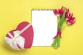 Bouquet of red tulips, gift box heart, notepad on yellow background Top view Flat lay Holiday greeting card Royalty Free Stock Photo