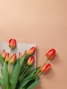 Bouquet of red tulips with kraft green envelope  on a natural beige color background. Mother`s Day, Easter, Valentine`s Day. Royalty Free Stock Photo