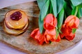 A bouquet of red tulips next to a stack of pancakes. Hot homemade cakes on wooden Board and flowers. Berry jam on top of pancakes
