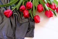 Bouquet of red tulips on white wooden background and silver bright dress with drapers. Elegant fashion flat lay. Fashion concept