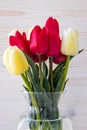 Bouquet of red and yellow tulips in glass vase on white wooden board background. Holiday gift card. Bunch of colorful flowers.