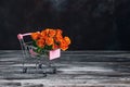 A bouquet of roses in a toy shopping cart on a dark rustic wooden table. Selective focus