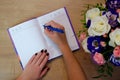 Bouquet of roses on wooden background, notebook and pencil in woman hand. Female hands writing in open notebook and bouquet of Royalty Free Stock Photo