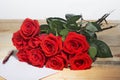 Bouquet of scarlet roses on a surface from wooden boards and the sheet paper for writing the text Royalty Free Stock Photo