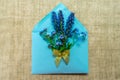 A bouquet of small blue flowers in a blue envelope decorated with a golden bow on a tablecloth made of natural flax.
