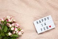 Bouquet of small roses on dusty pink blanket, lightbox with inscription Happy 14 FEB that means Valentine`s Day. Flat lay. Top