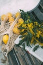 A Bouquet Of Spring Yellow Flowers And A String Bag With Lemons Lie On A Bench In A Snowy Park. Yellow Mimosa
