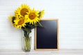 A bouquet of sunflowers in a vase and empty chalkboard against the background of a white brick wall Royalty Free Stock Photo