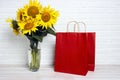A bouquet of sunflowers in a vase with red paper shopping bag against the  white brick wall Royalty Free Stock Photo