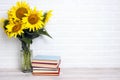 A bouquet of sunflowers in a vase with stack of books against the white brick wall Royalty Free Stock Photo