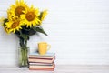 A bouquet of sunflowers in a vase with Stack of books and yellow mug against the white brick wall Royalty Free Stock Photo