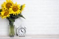 A bouquet of sunflowers in a vase and vintage alarm clock against the white brick wall Royalty Free Stock Photo