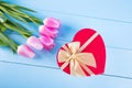Bouquet of tender pink tulips with red gift box in form of heart on light blue wooden background Royalty Free Stock Photo
