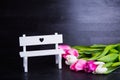 Bouquet of tender pink tulips with white bench on black wooden b Royalty Free Stock Photo
