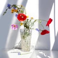 Bouquet of three red poppy flowers and different wildflowers in crystal vase with water on white table with contrast sun light and Royalty Free Stock Photo