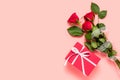 Bouquet of three red roses and gift box with white bow knot on pink background. Mother`s, women`s or Valentine`s day greeting. Royalty Free Stock Photo