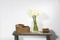 Bouquet of three white lilies in a tall glass vase on a beige vintage bench against a gray wall. Wooden boxes of different sizes Royalty Free Stock Photo
