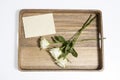 A bouquet of three white roses ion a wooden tray with an evelope