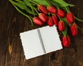 Bouquet of tulips, blank notebook, pen on the wooden background