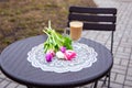 Bouquet of tulips lies on the table near a cup of coffee in the courtyard of the cafe