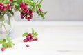 Bouquet of twigs with red ripe lingonberries in glass on light background. traditional vegetation