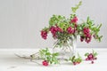 Bouquet of twigs with red ripe lingonberries in a glass on a light background.