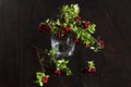 Bouquet of twigs with red ripe lingonberries in glass on wooden background. traditional vegetation