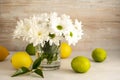 Bouquet of white chrysanthemums in glasswith whole lemons and limes. Abstract floral and fruits rustic background.