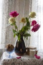 A bouquet of roses in a vintage vase on a lace tablecloth , next to books, a glass of milk and a bowl of cookies