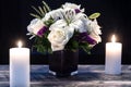Bouquet of white flowers in a purple vase, white candle on a wooden boards. Vintage home decor dark tones. Condolence card Royalty Free Stock Photo