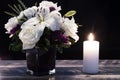 Bouquet of white flowers in a purple vase, white candle on a wooden boards. Vintage home decor dark tones. Condolence card Royalty Free Stock Photo