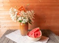 Bouquet of white hydrangeas and orange lilies in clay vase, watermelon in clay bowl near