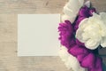 A bouquet of white and lilac peonies on a wooden board with a white sheet for greeting card. Mock up. Toned image.