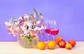 Bouquet of white lilies with purple spots in glass round vase, glasses of rose wine and fresh fruits on wooden table. Purple Royalty Free Stock Photo